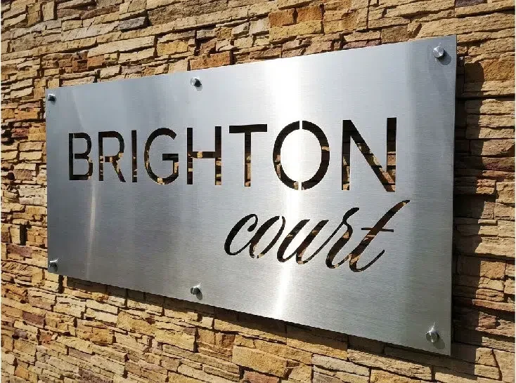 Brushed metal flat panel with stencil-cut lettering mounted on stone using circular standoffs